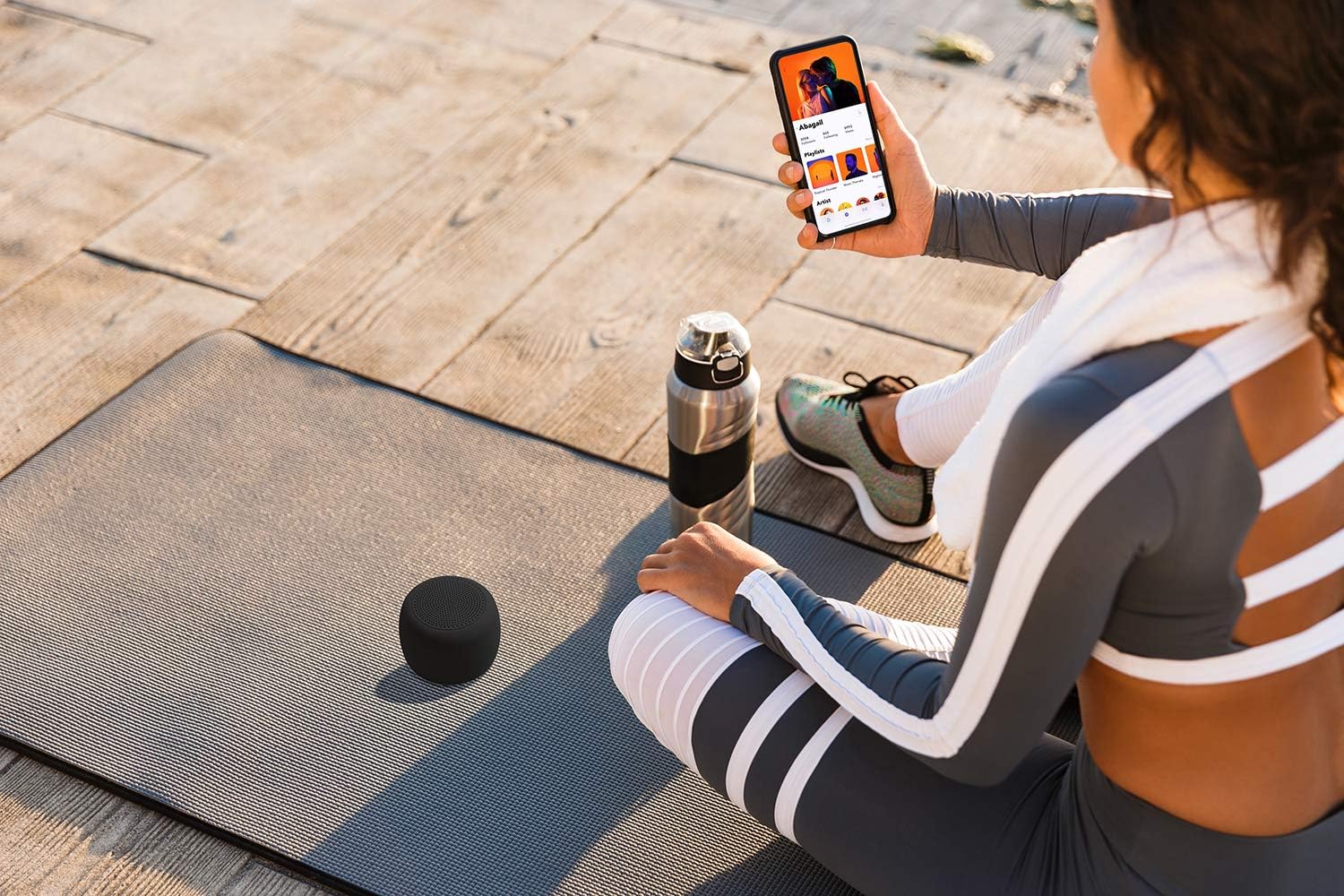 Person using a smartphone with the Juice Jumbo Marshmallow speaker nearby on a yoga mat