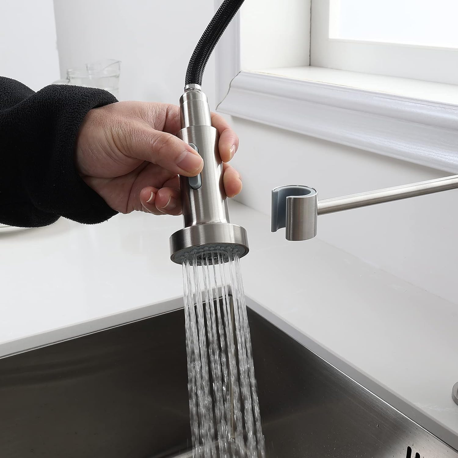 Hand demonstrating the pull-down spray head in use, showing water spraying from the nozzle.