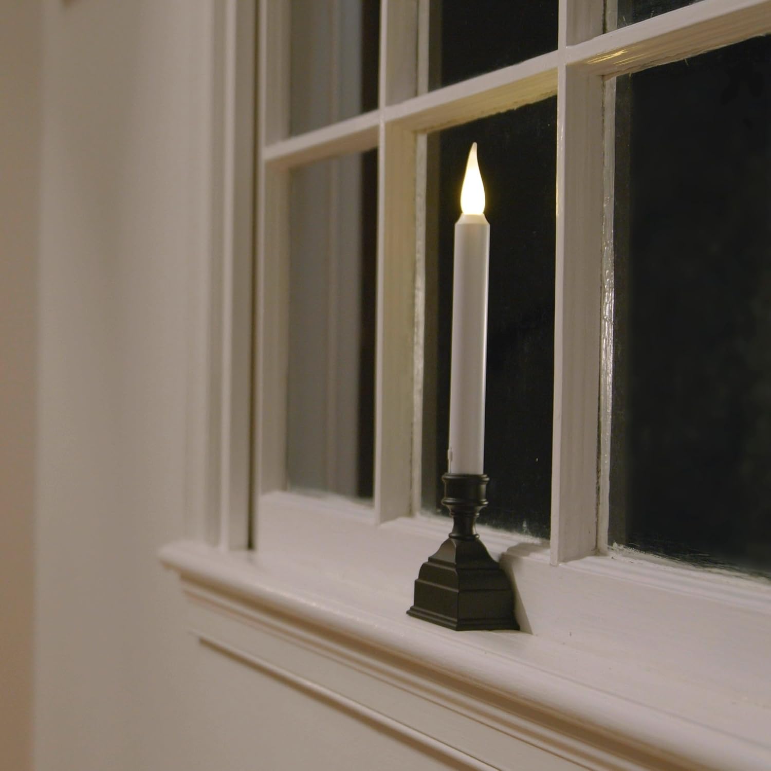 Image of an LED window candle placed on a windowsill, illuminated at night.