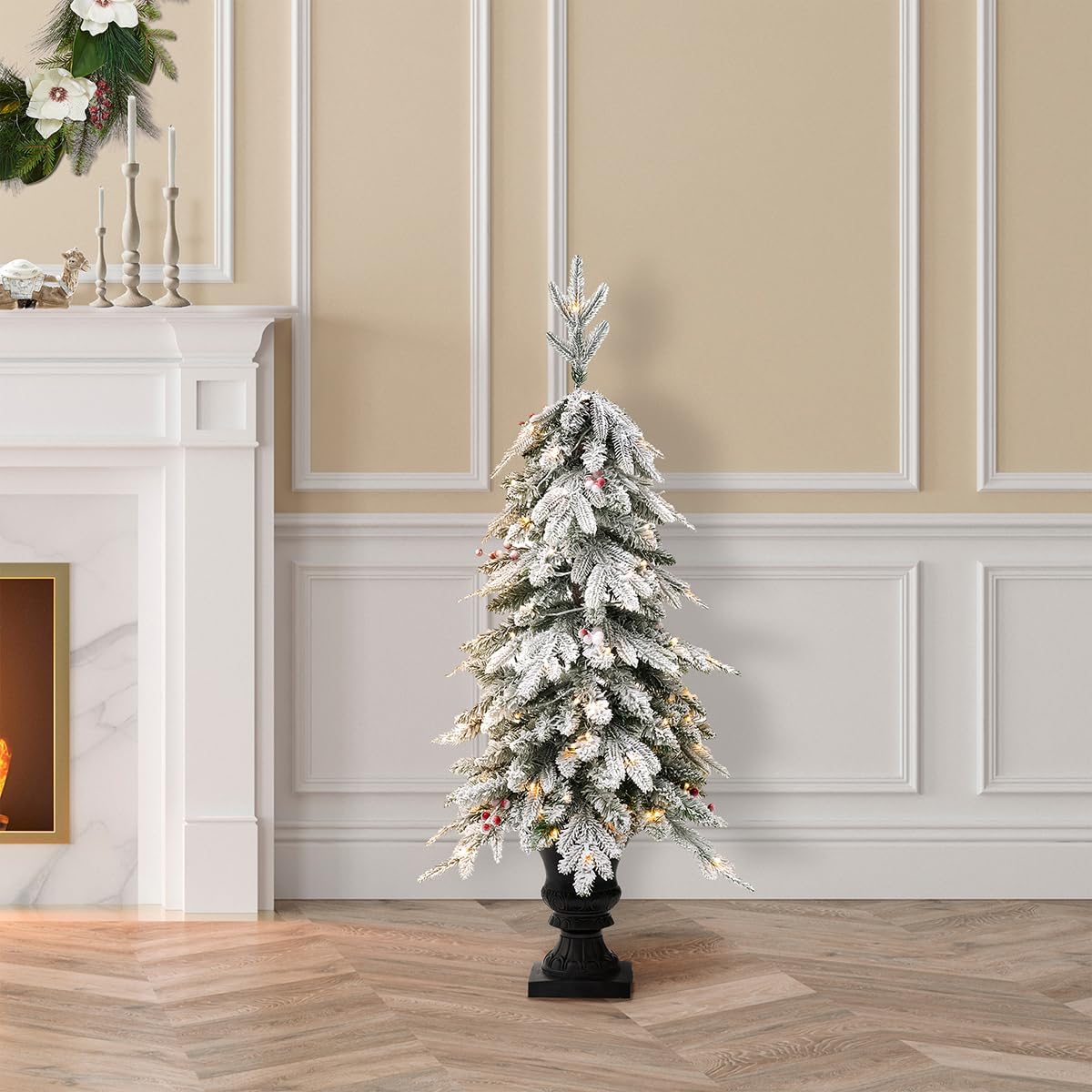 A single Glitzhome 4ft flocked Christmas tree with warm white lights and red berries, in an urn base, placed indoors next to a white fireplace.