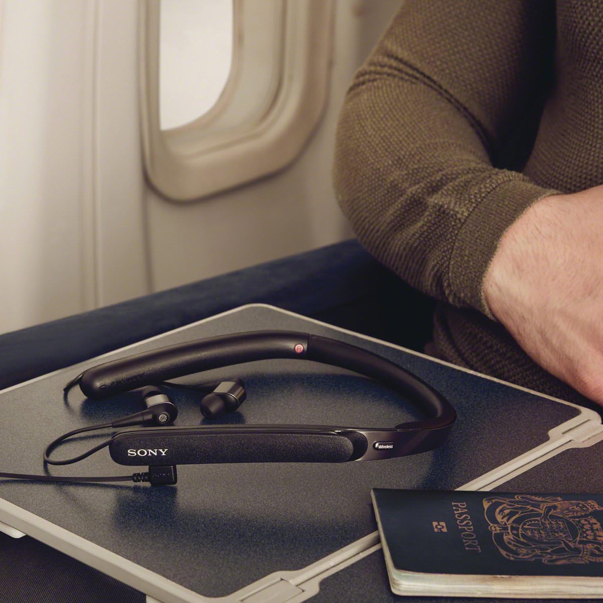 Sony WI-1000X headphones folded on an airplane tray table, connected via cable, with a passport nearby.