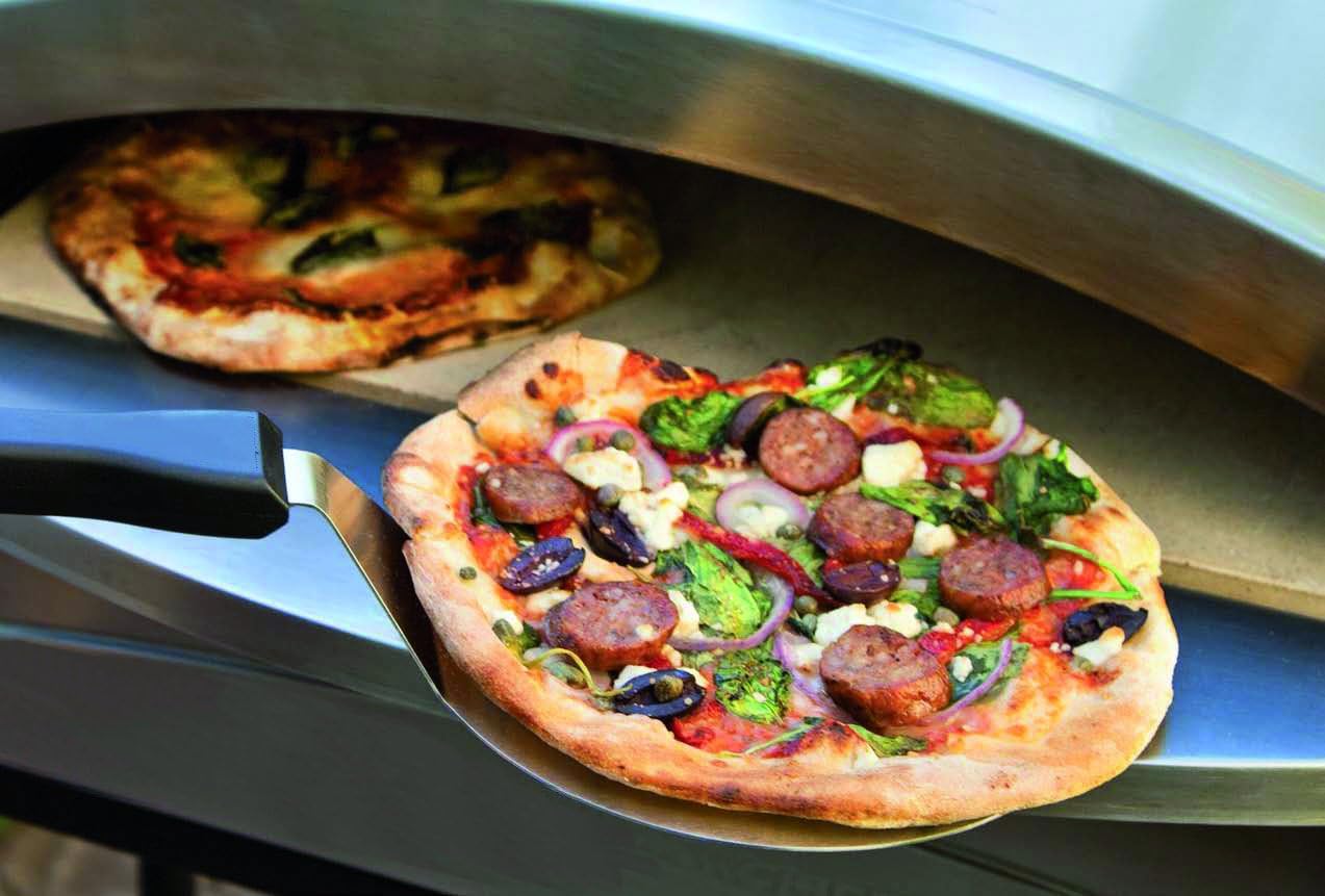 A freshly cooked pizza being removed from the KEMPER pizza oven with a metal spatula