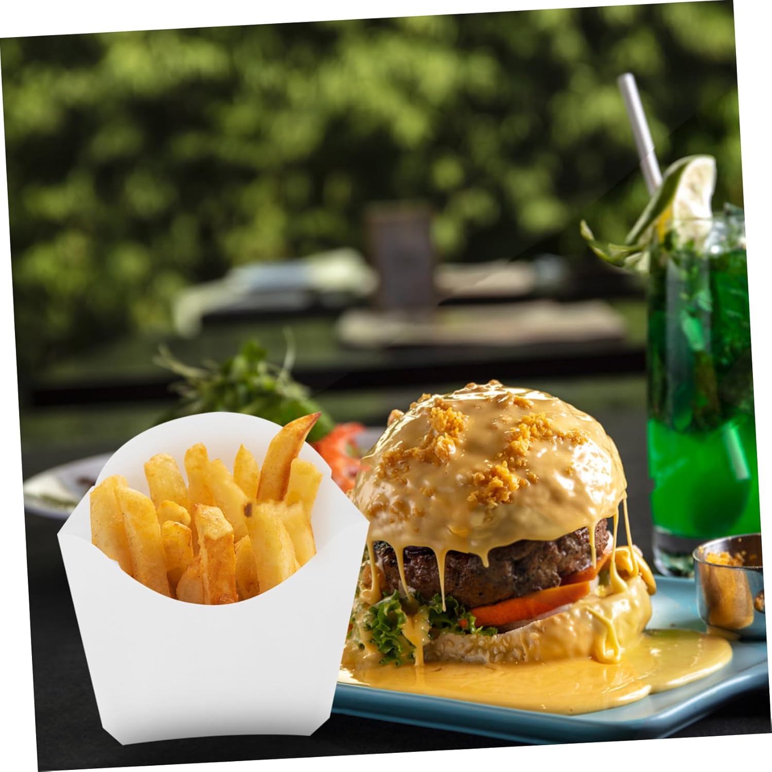 A white paper snack box filled with French fries, positioned next to a large cheeseburger and a drink.