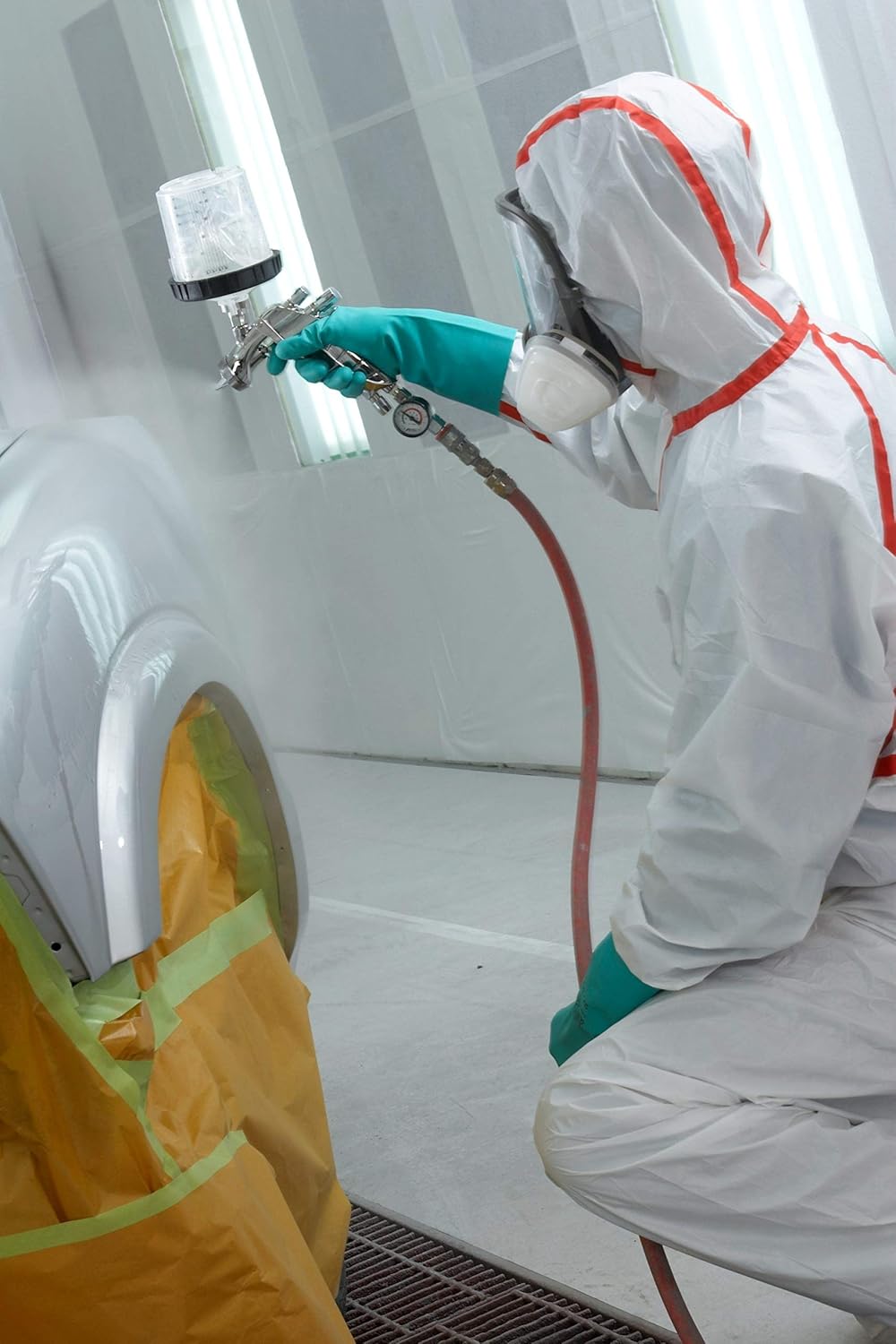 Worker kneeling and spray painting while wearing the 3M coverall and respirator
