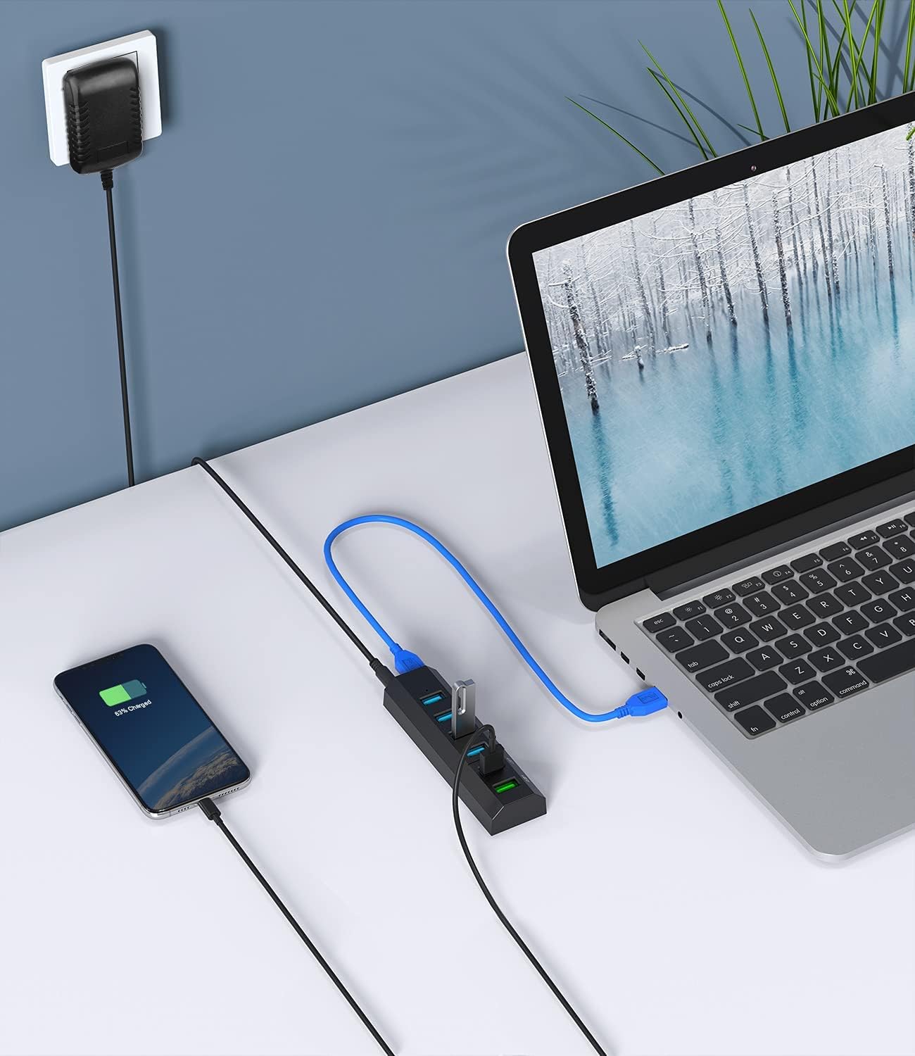 Vansuny USB 3.0 Hub connected to a laptop via a blue USB cable, with a smartphone charging from one of the hub's ports. The power adapter is plugged into a wall outlet.