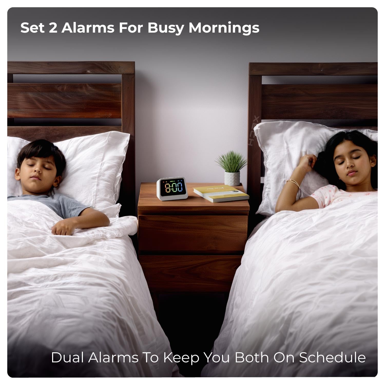 Two children sleeping in separate beds with the Xech Prism Pro alarm clock on a bedside table between them, illustrating its dual alarm feature