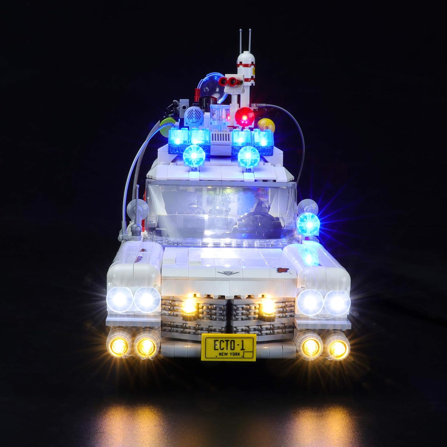 Front view of the LEGO Ghostbusters ECTO-1 model with the YEABRICKS LED Light Kit activated, showing bright headlights and roof lights.