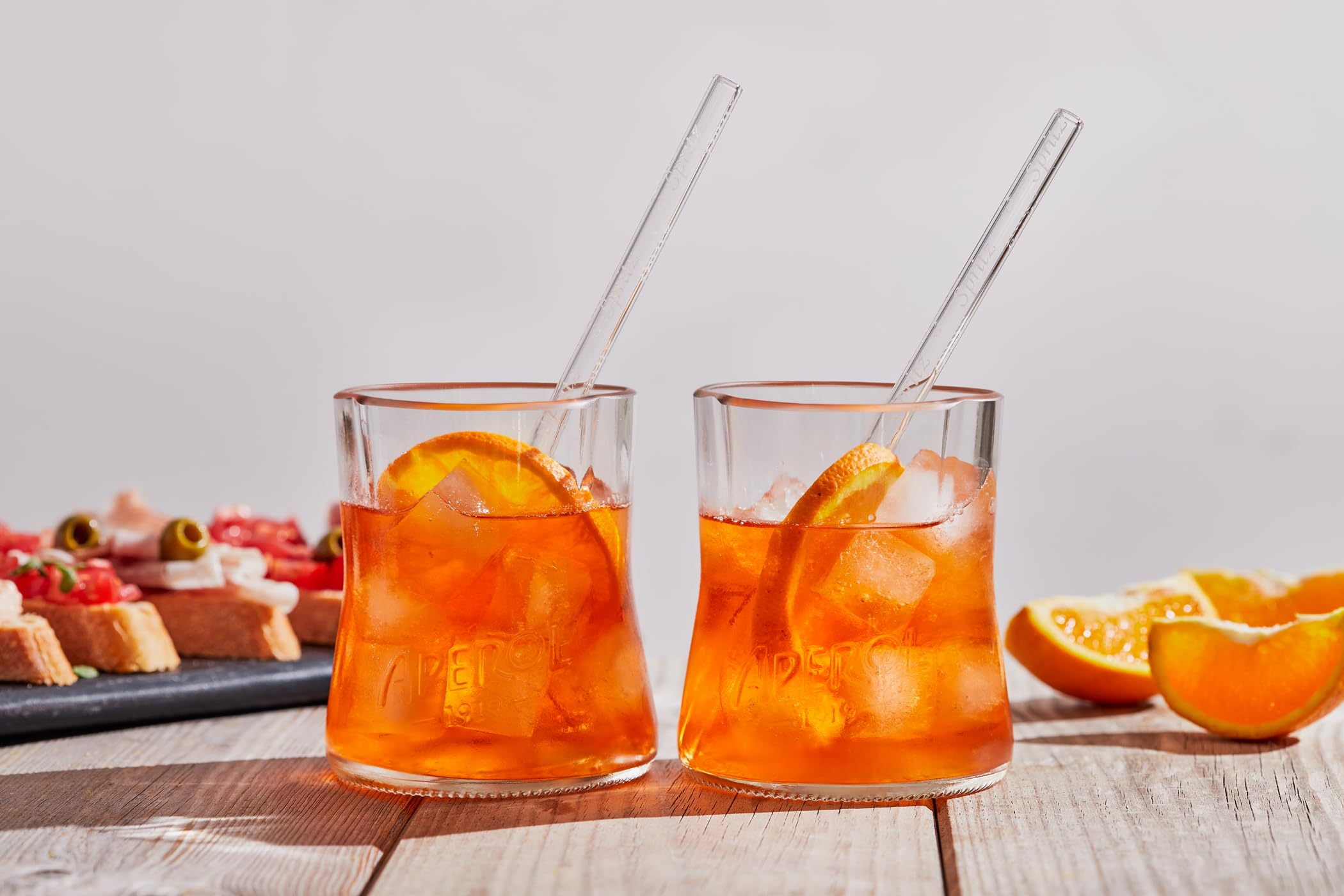 Aperol Spritz Set aus recycelten Flaschen: zwei Glaser mit kunstvoll geformten Randern und zwei Glasstronhhalme