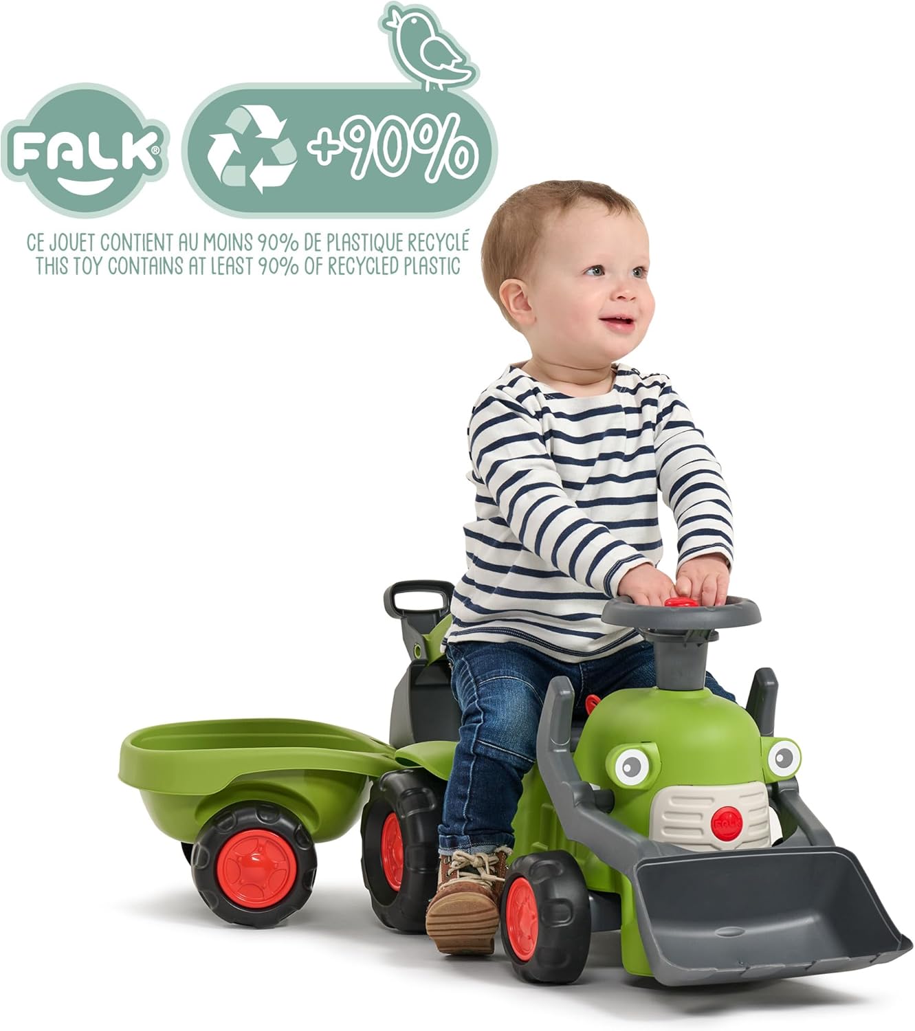A happy toddler sitting on the Falk Claas Backhoe Loader, which is green with red wheels and a grey shovel. The image highlights that the toy contains at least 90% recycled plastic.