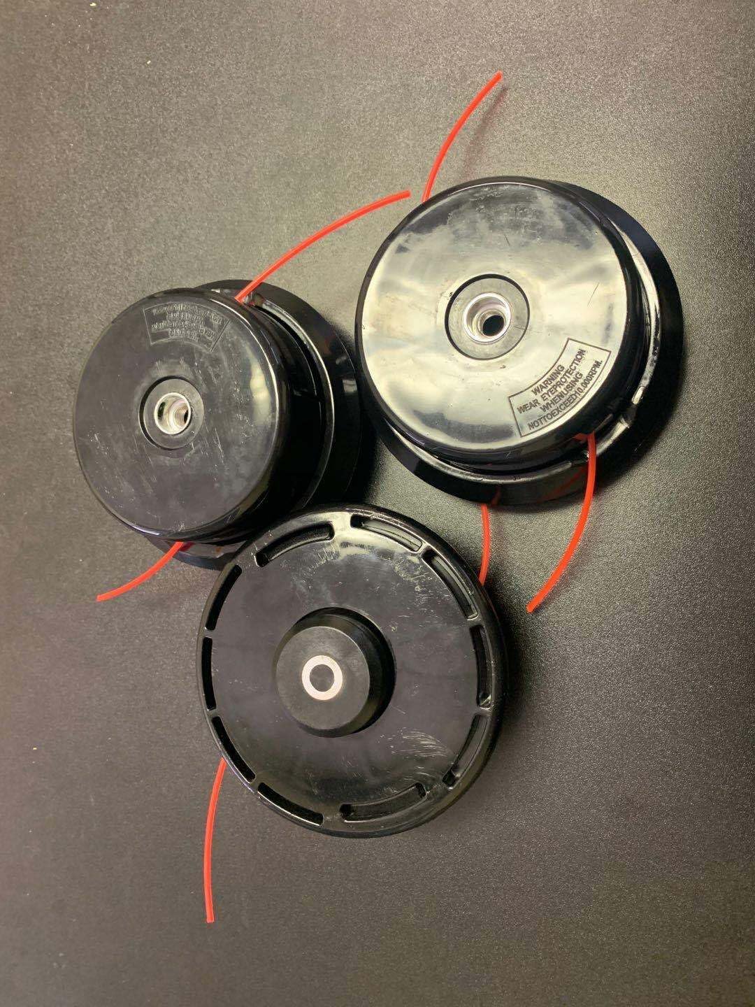 Three black string trimmer heads with red lines, bottom view showing warning labels