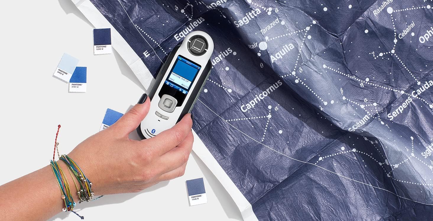 A hand holding the Pantone CAPSURE device over a patterned surface to capture a color.