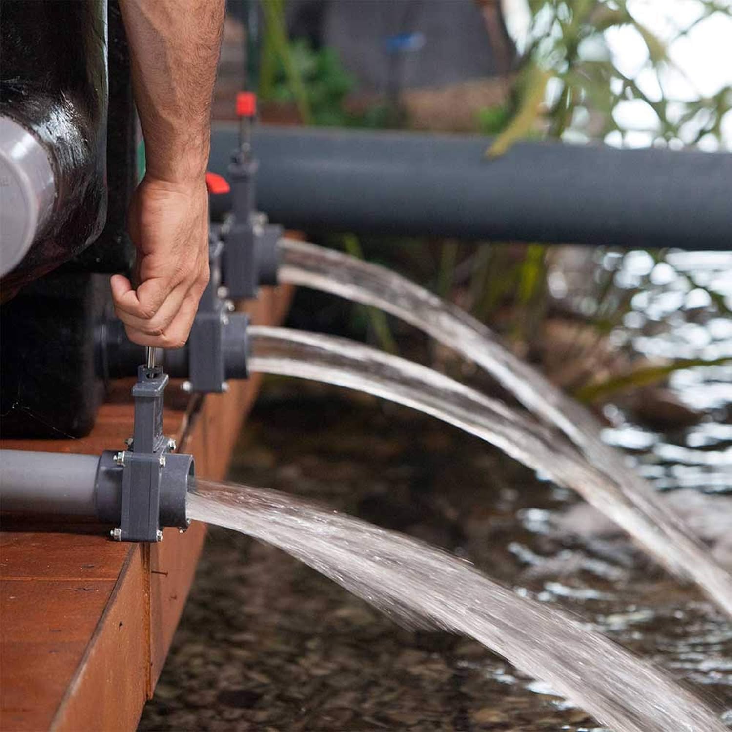 A hand operating one of the drain valves on the Heissner Apollo XXL PRO pond filter, showing water being discharged.