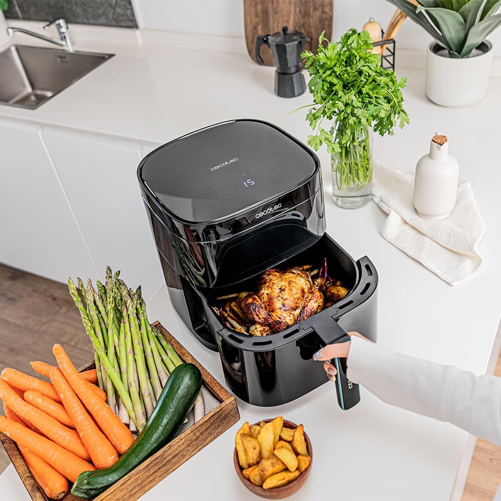 A woman pulling out the cooking basket from the Cecotec Cecofry DuoHeat 6000 Air Fryer, revealing a whole roasted chicken and vegetables.