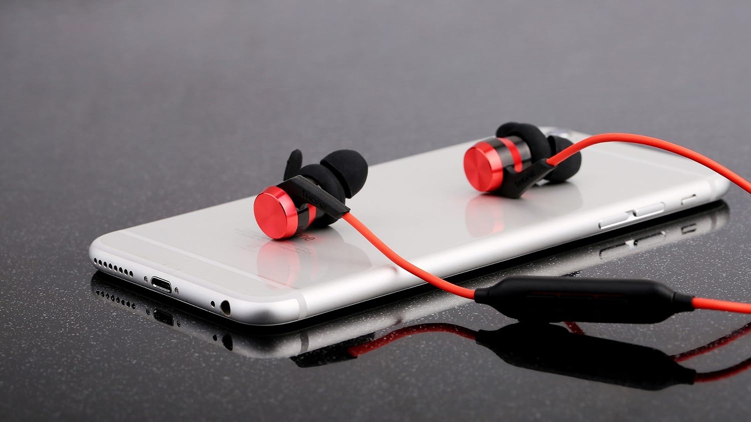 1MORE iBFree wireless Bluetooth headphones in red and black, resting on a silver smartphone.