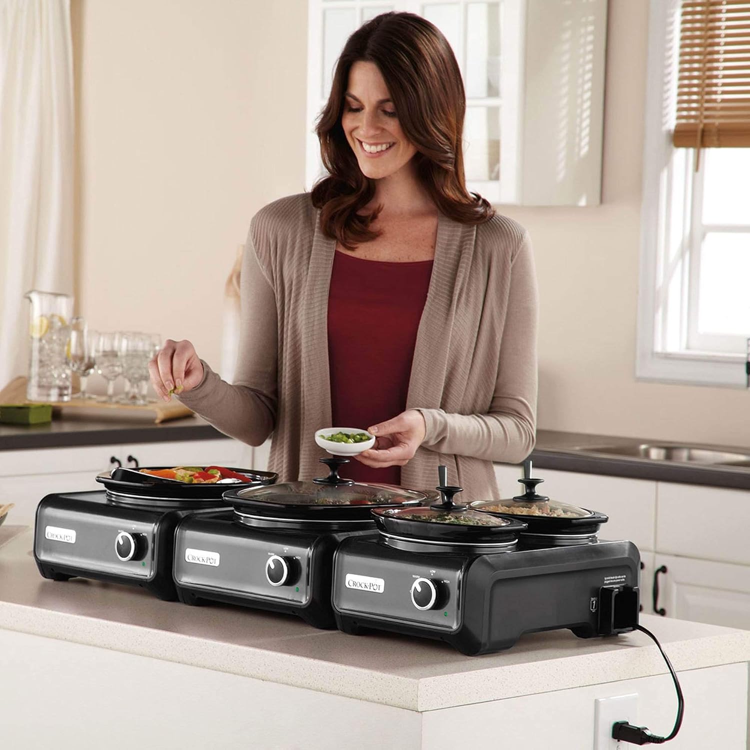 A woman placing a small dish of garnish into one of the Crock-Pot Hook Up units, which are arranged on a counter.