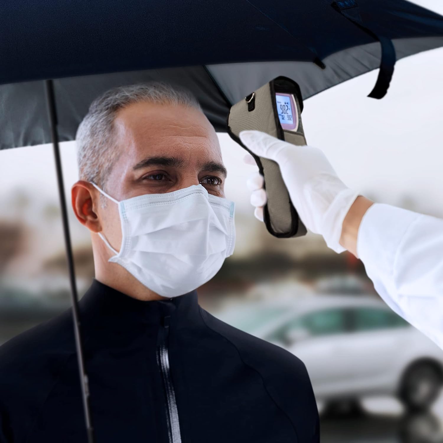 Person using the thermometer while it is inside its utility case, under an umbrella in the rain, demonstrating its protection.