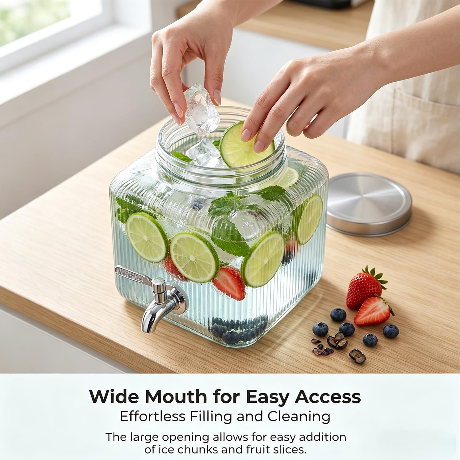 Hands adding ice and lime slices to the wide mouth of the glass drink dispenser.