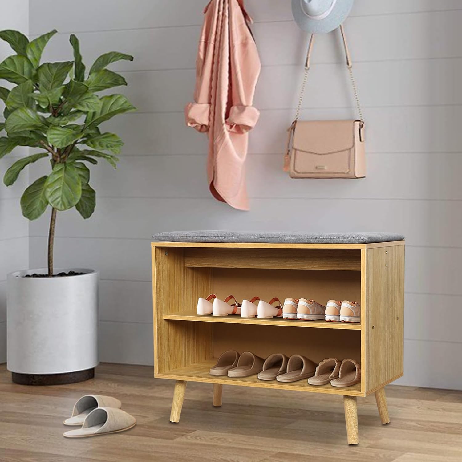 The shoe storage bench placed in an entryway with a plant and coat rack, demonstrating its use as both storage and seating.