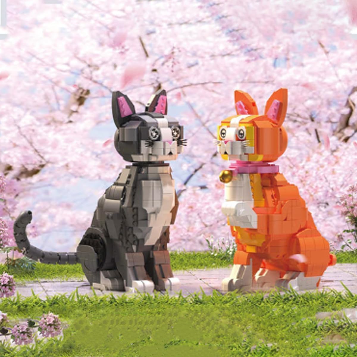 Two JOMIOD cat building block models, orange and grey, under cherry blossoms.