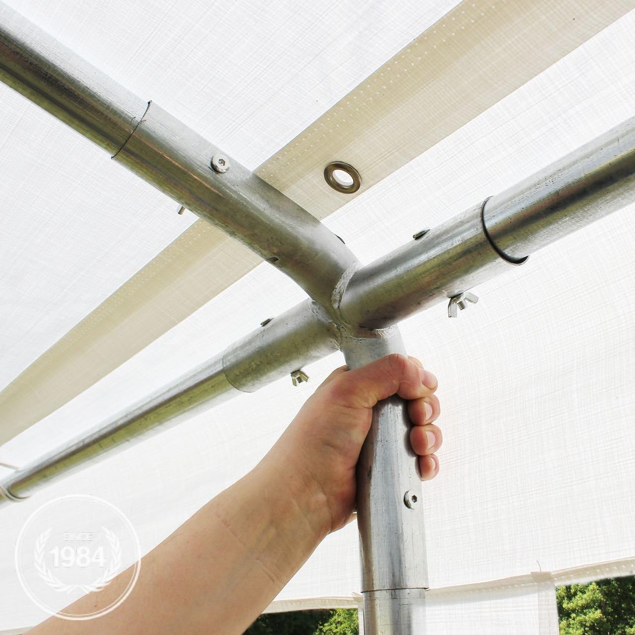 Close-up of a hand holding a galvanized steel pole connected to a frame joint with bolts