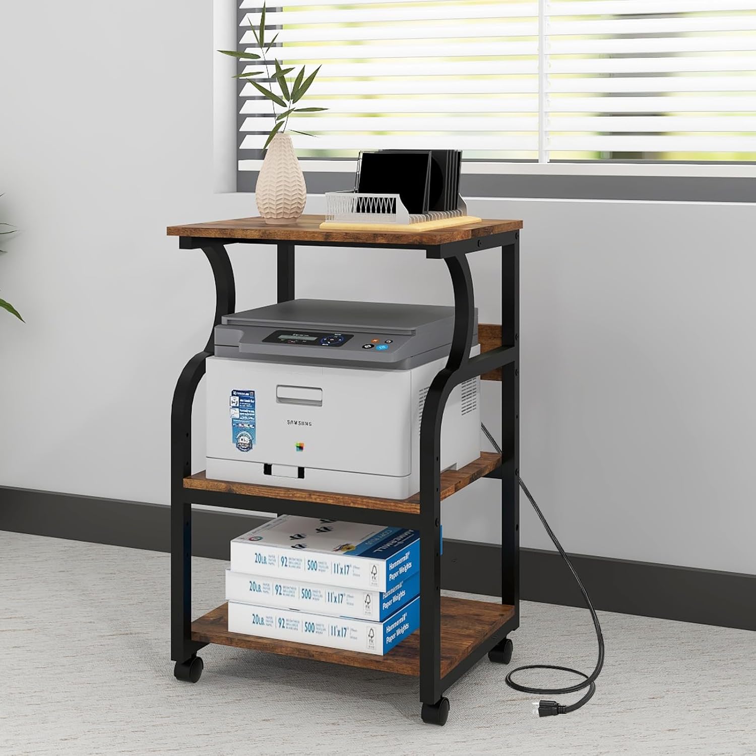 Natwind 3 Tier Printer Stand in a home office setting, holding a printer and paper, with the power cord from the built-in outlets plugged into a wall.