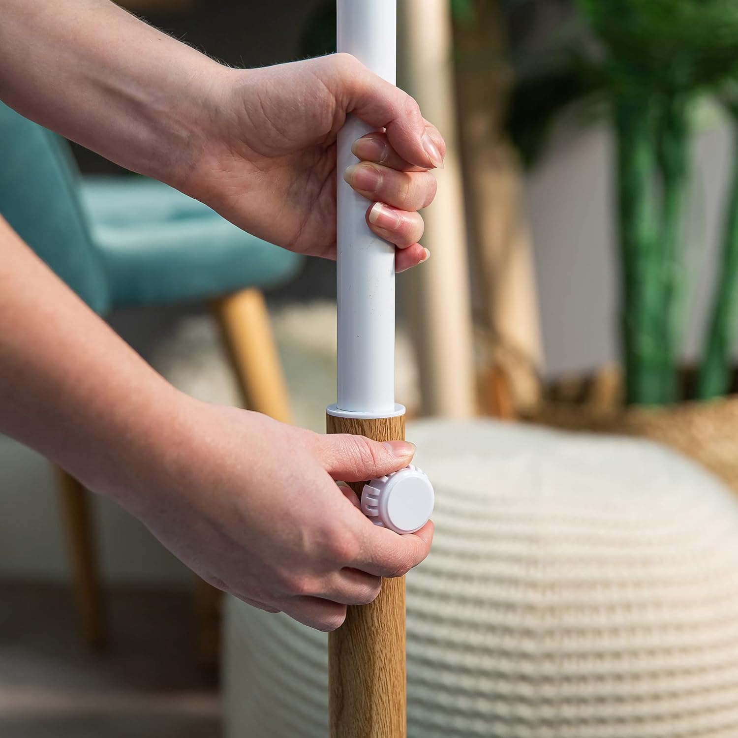 Hands adjusting the height of the fan pole by loosening and tightening a white knob on the wooden-effect section of the stand.