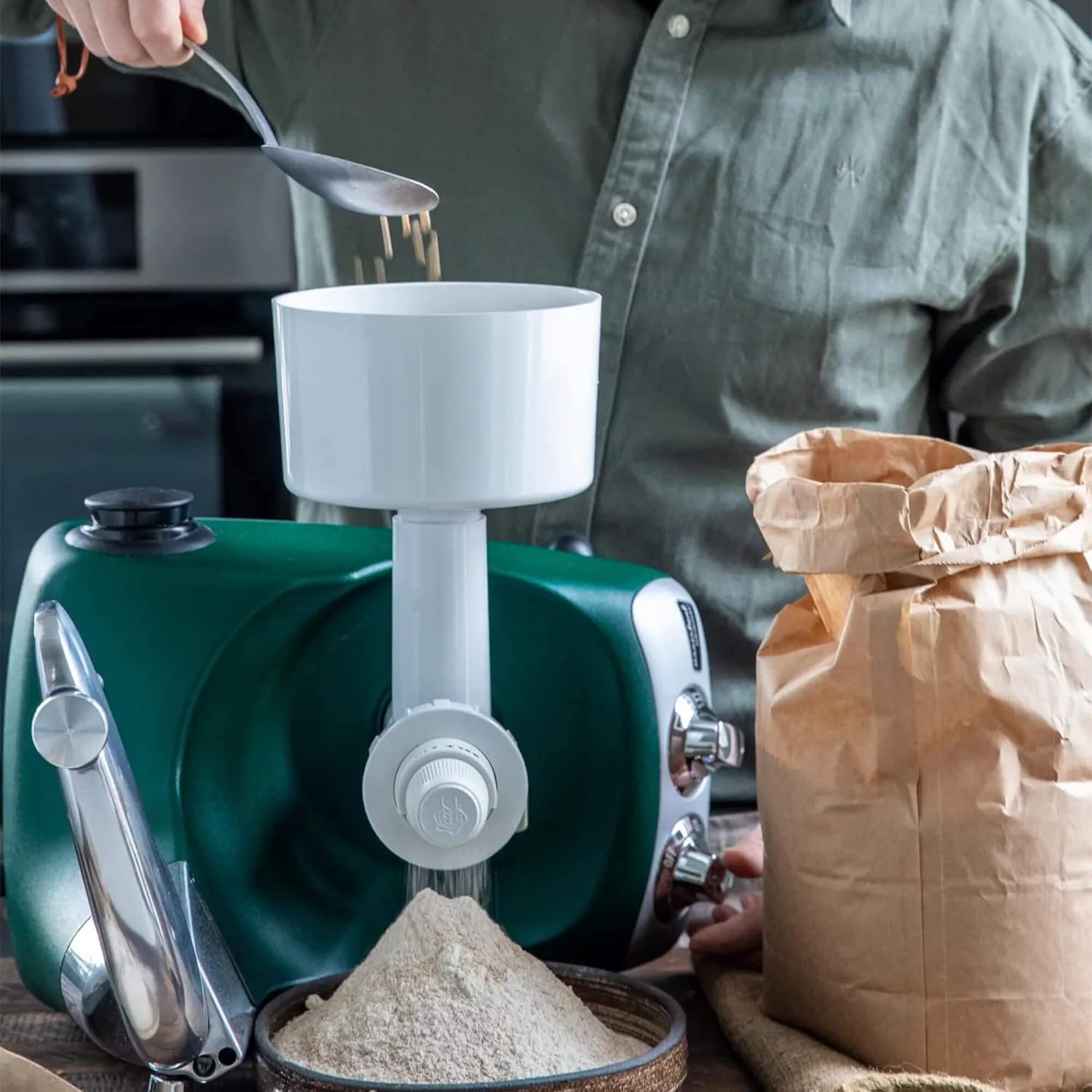 Person adding grain to the ANKARSRUM Grain and Spice Mill hopper with a spoon.