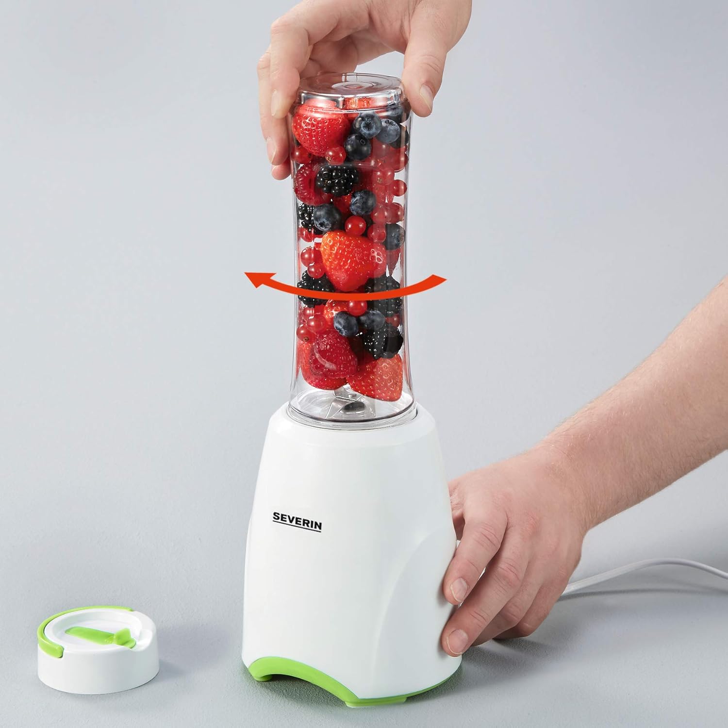 Hands placing a bottle filled with berries onto the blender base
