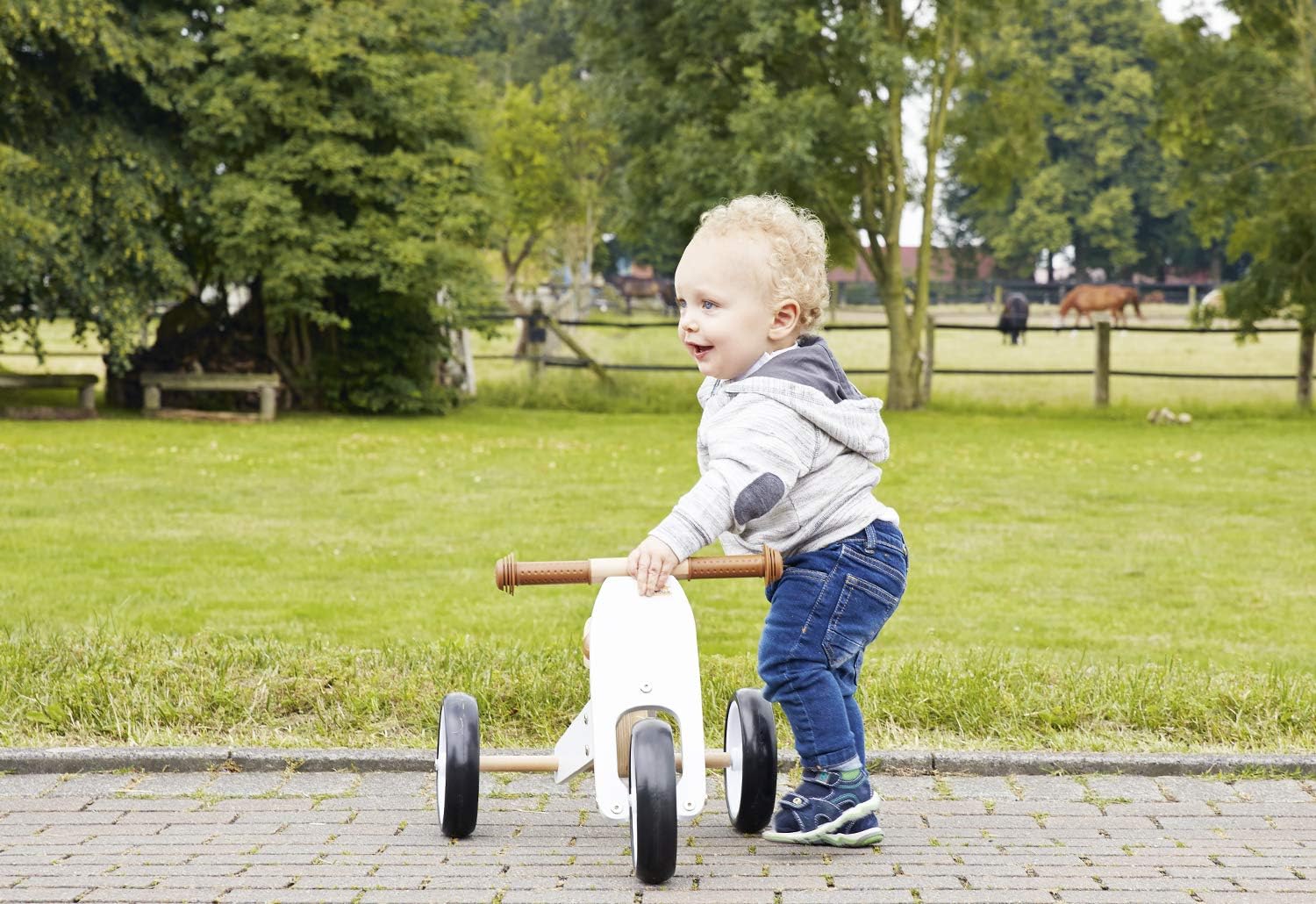 A young child pushing off on the PINOLINO Mini Tricycle 'Charlie' in a trike configuration outdoors.