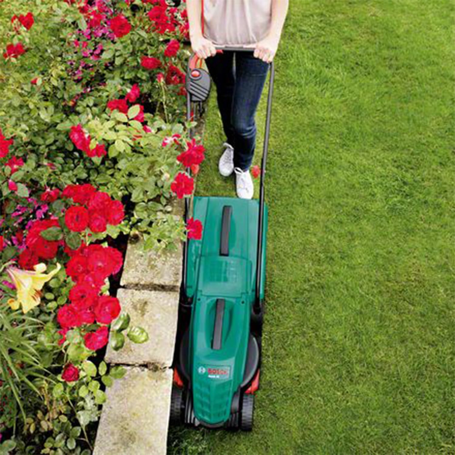 Una sobrecàrrega view of the Bosch Rotak 32 electric lawn mower being used to cut grass, showing its compact design and effective cutting path.