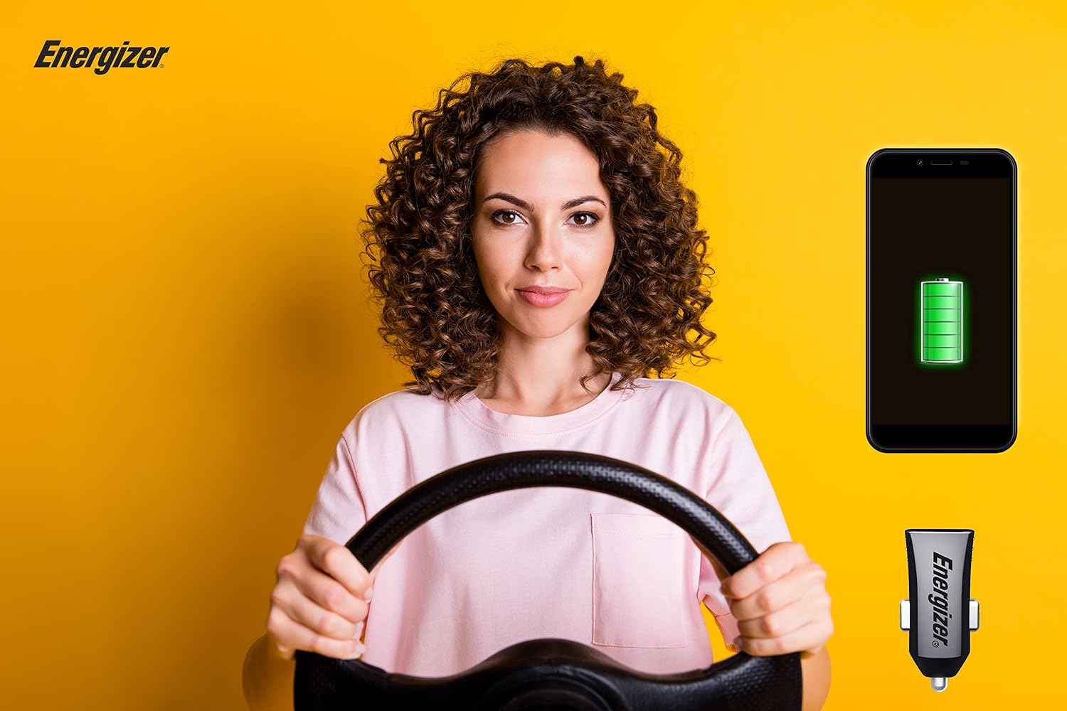 A woman driving, with a smartphone displaying a charging battery icon and the Energizer D12 car charger visible.