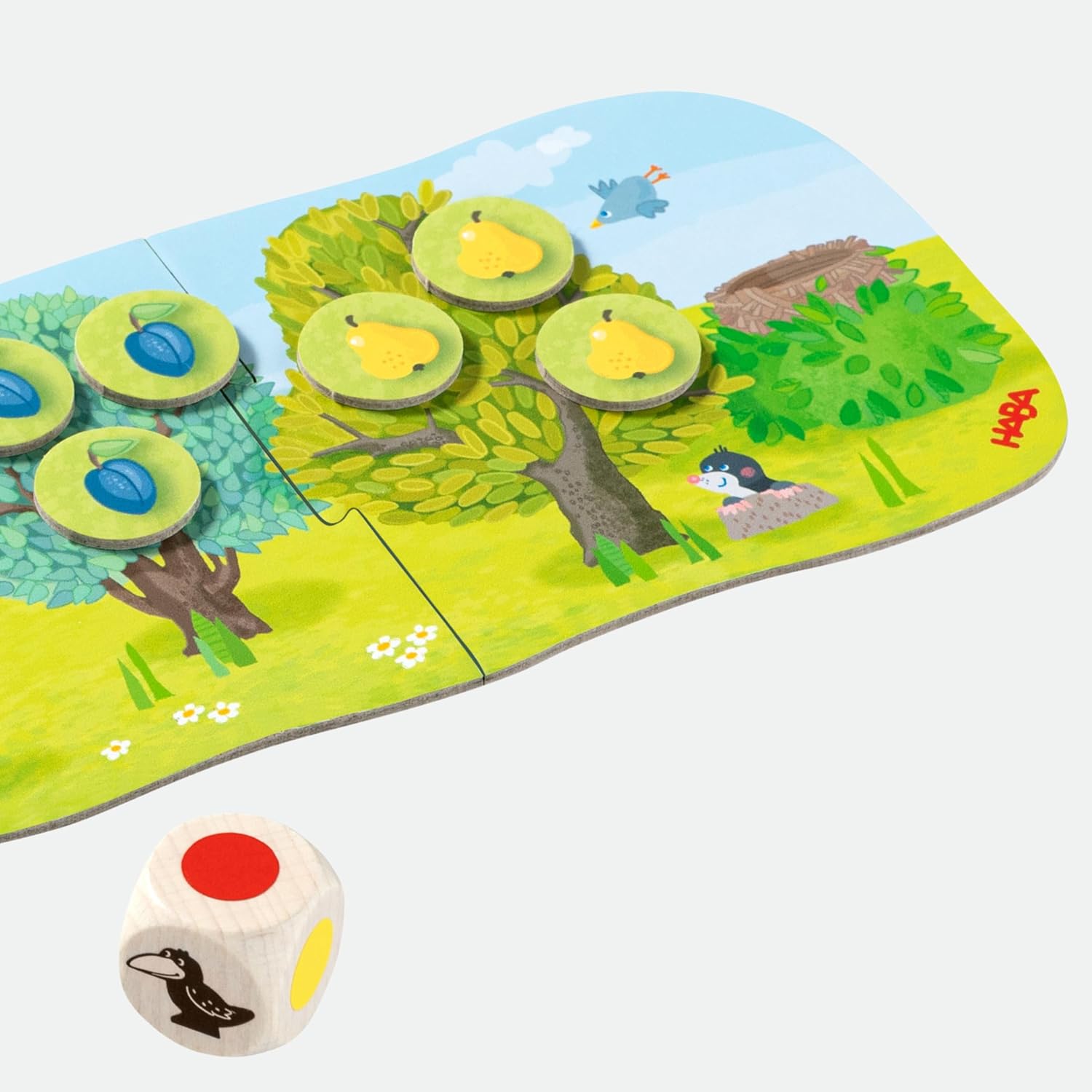 HABA Super Mini Orchard game components laid out: game board pieces with fruit tokens, a wooden crow figure, and a color die.