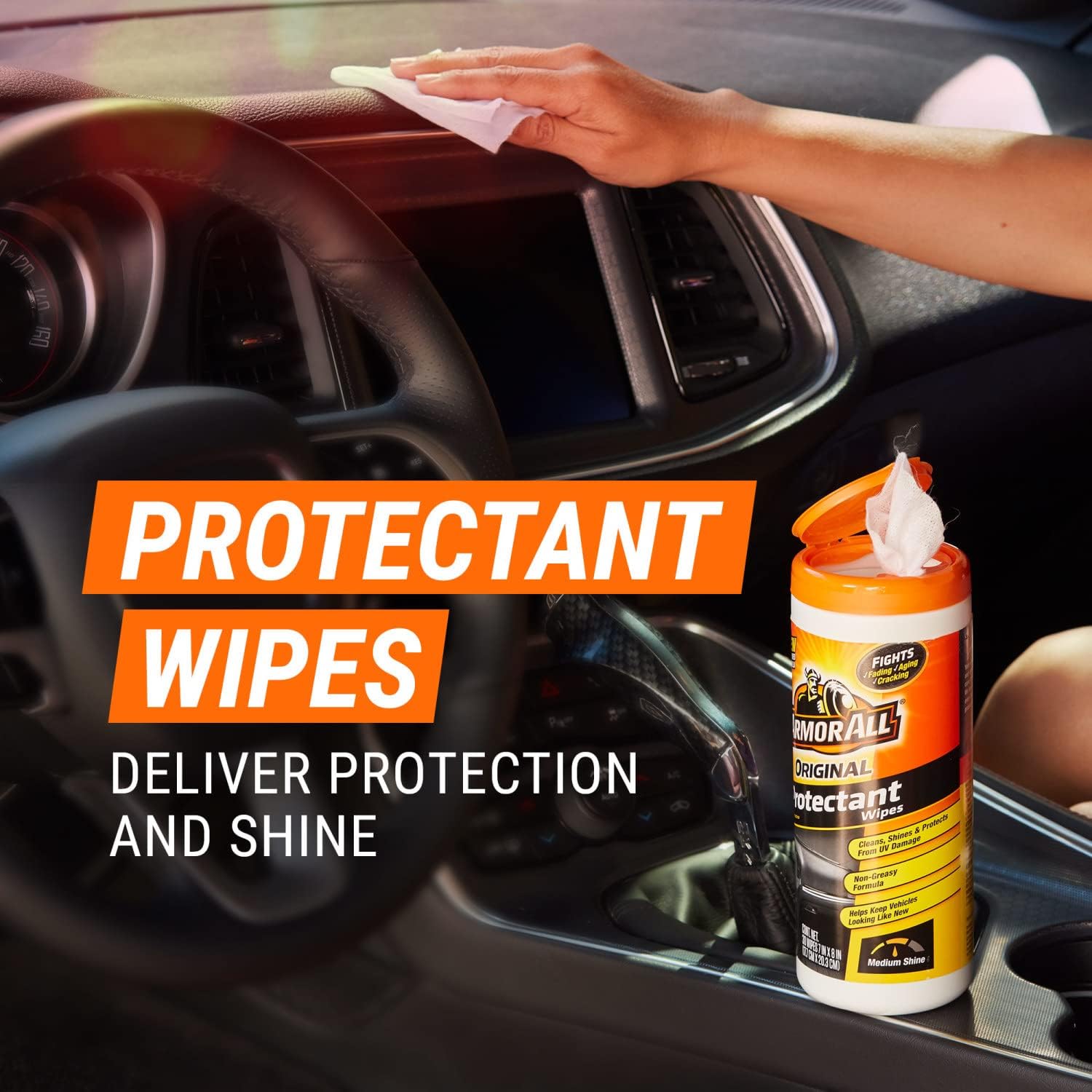 Hand wiping a car dashboard with an Armor All protectant wipe.
