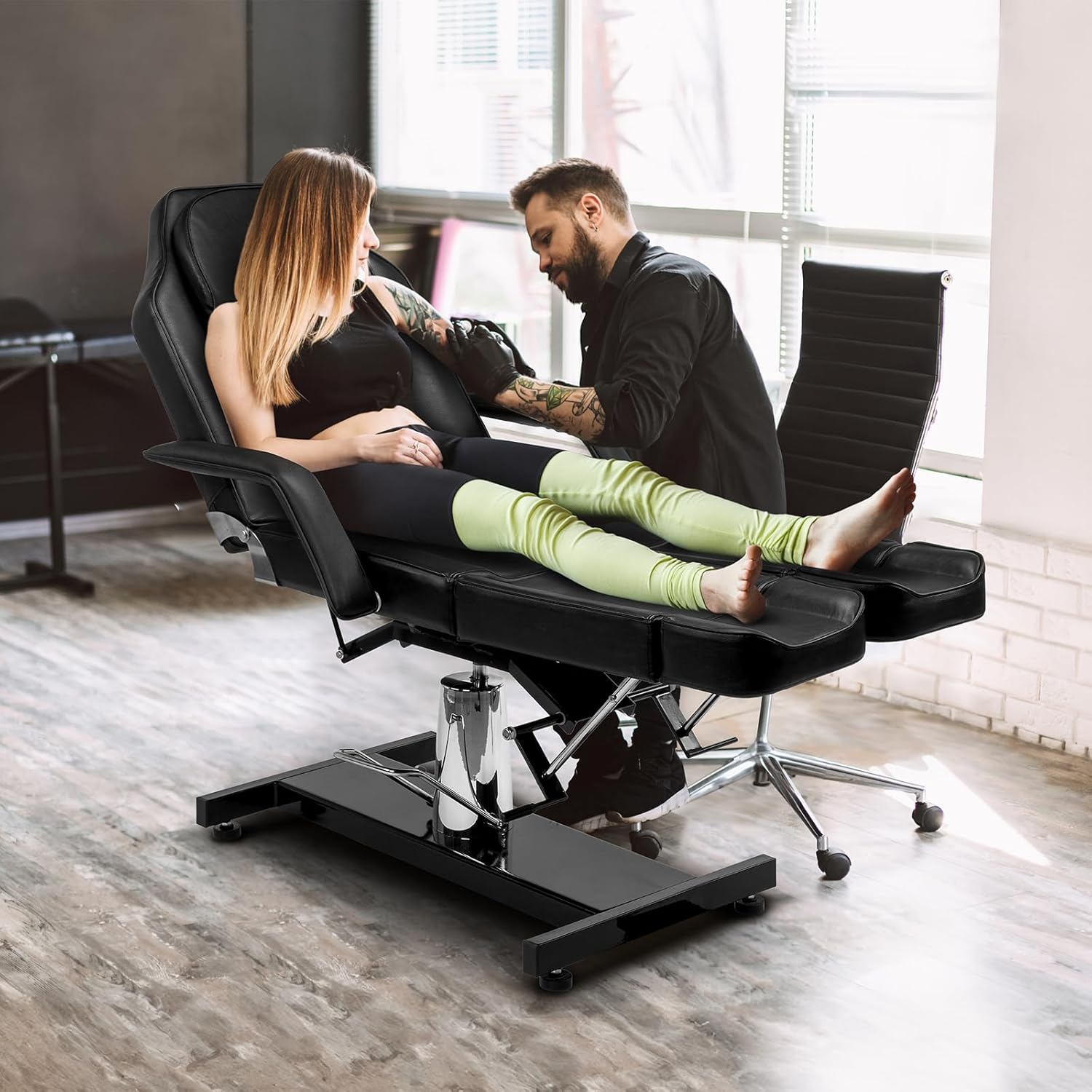 Image showing the OmySalon treatment chair in use, with a tattoo artist working on a client's arm, demonstrating its practical application.