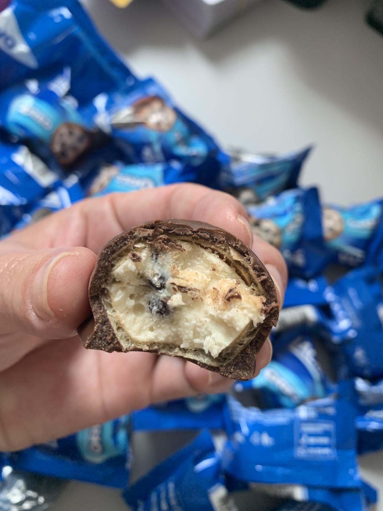 Close em uma mão segurando um bombom Lacta Oreo cortado ao meio mostrando o recheio