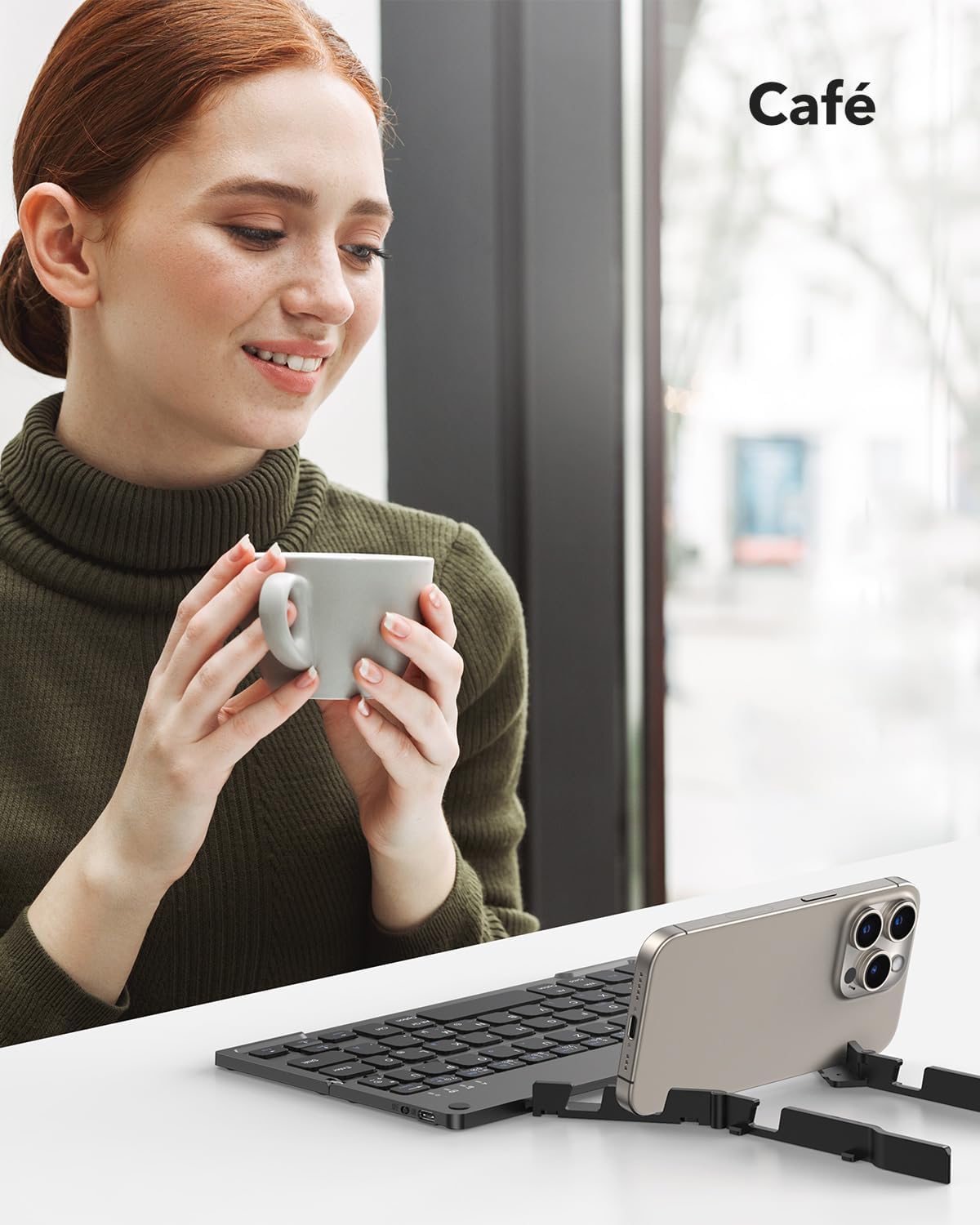 A person using the TECURS KB195 keyboard with a smartphone on its stand in a cafe setting.