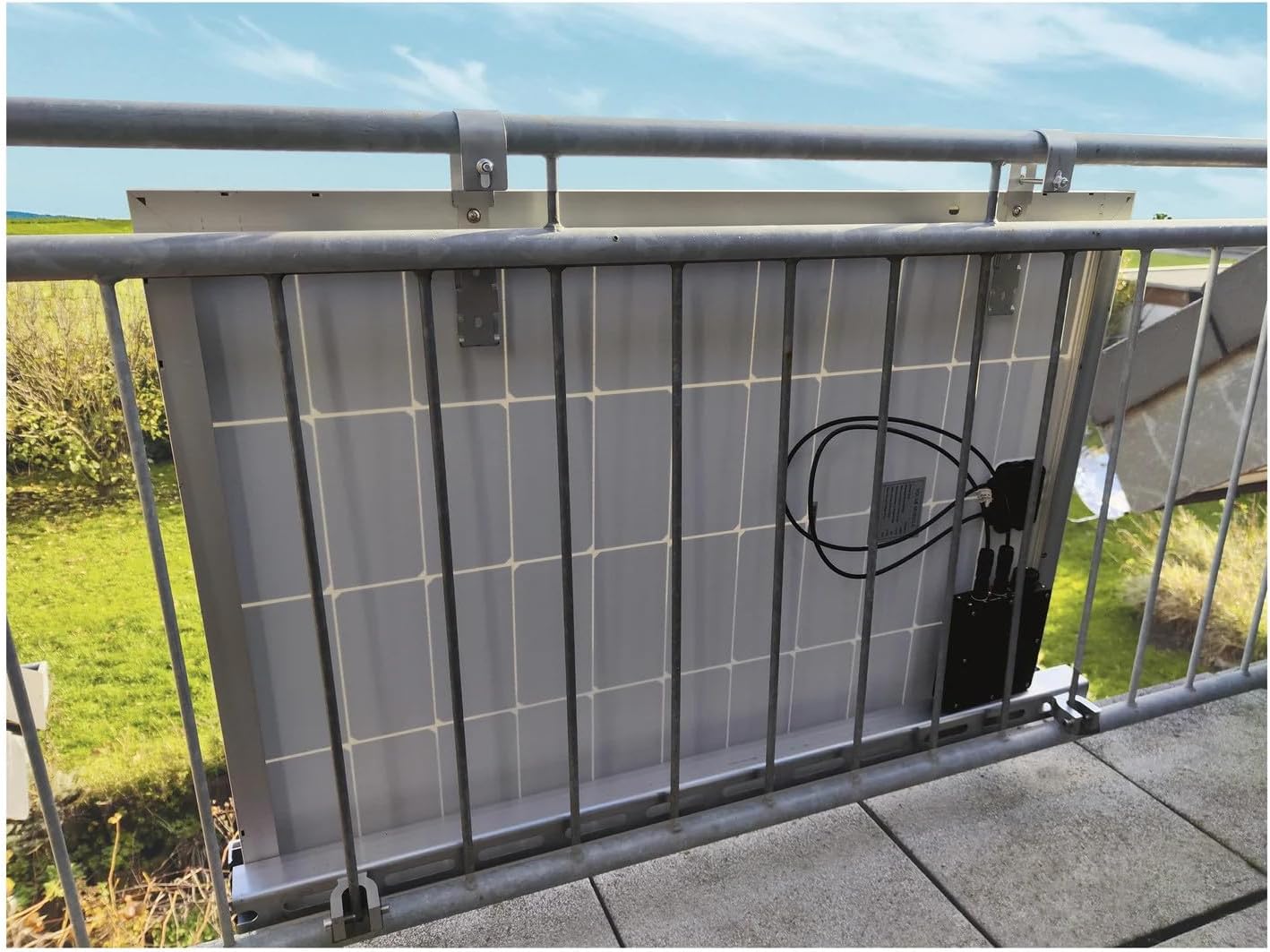 Rear view of a solar panel showing the micro inverter and cables connected, mounted on a balcony railing.
