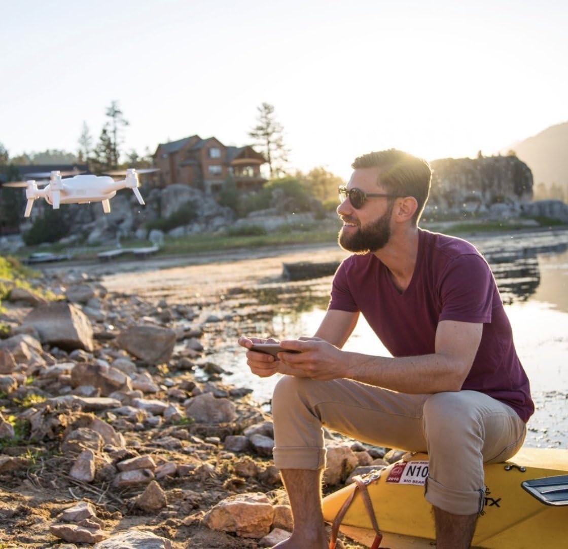 A person sitting by a lake, operating the Yuneec Breeze drone with a smartphone.