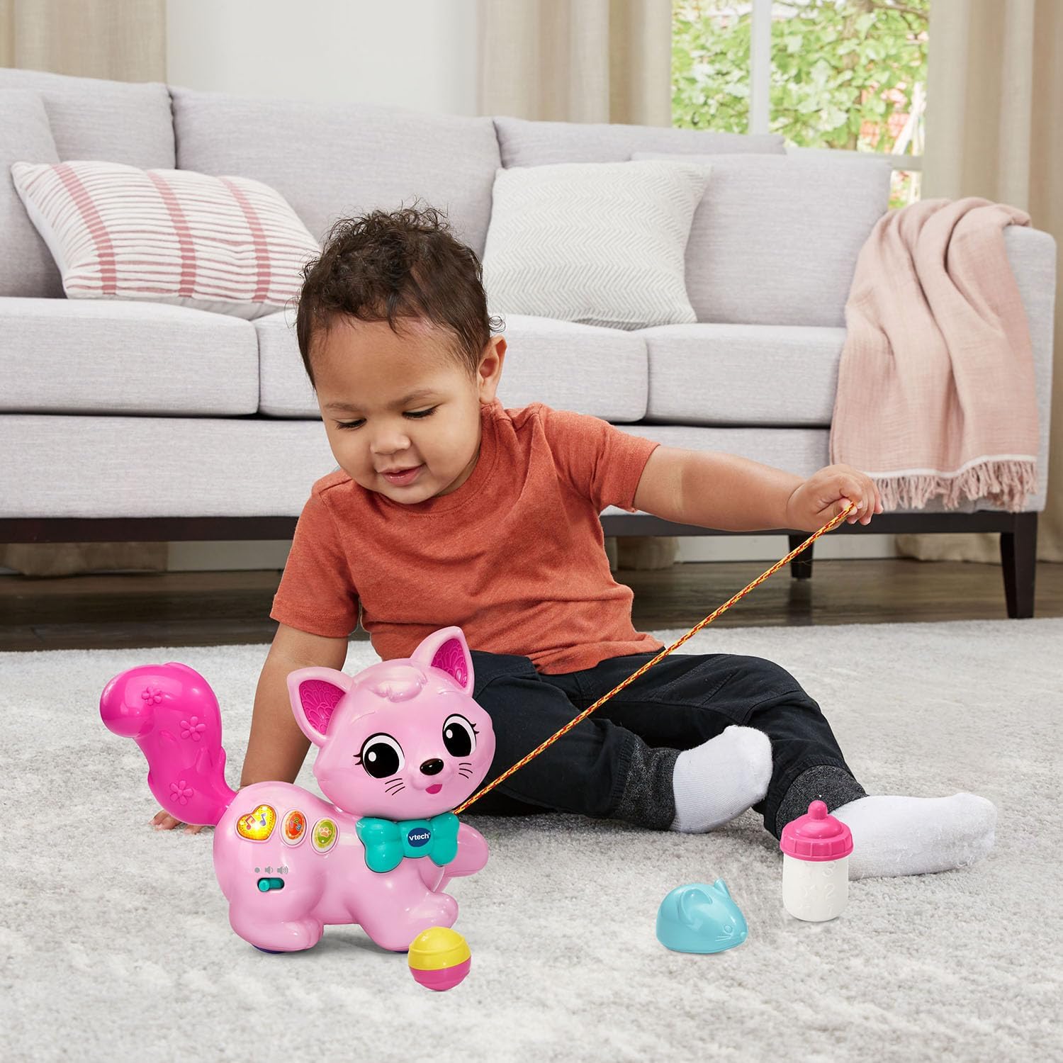 A child playing with the VTech Sing and Stroll Kitty and its accessories, including a bottle, mouse, and ball.