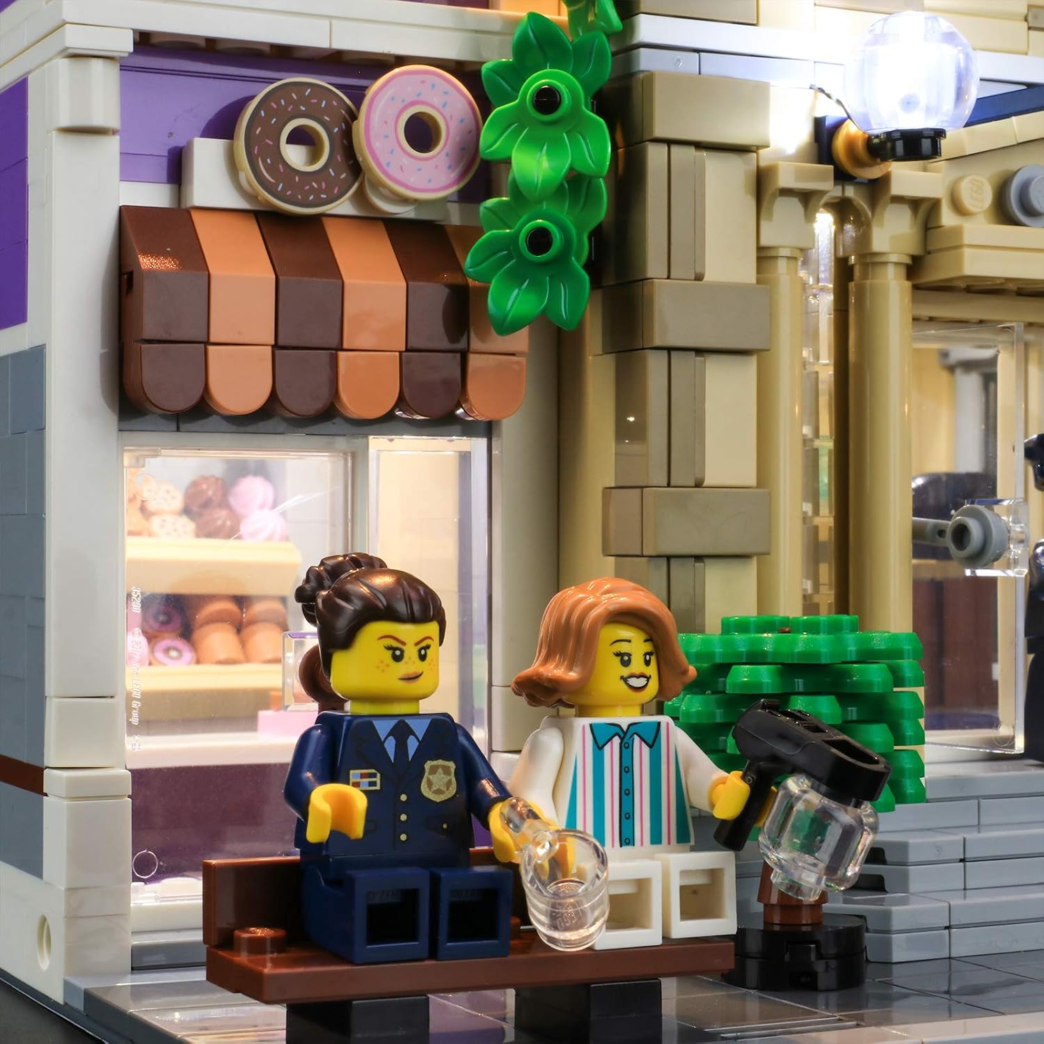 Close-up of the illuminated donut shop and police figures in the LEGO 10278 Police Station, highlighting the detailed lighting effects.