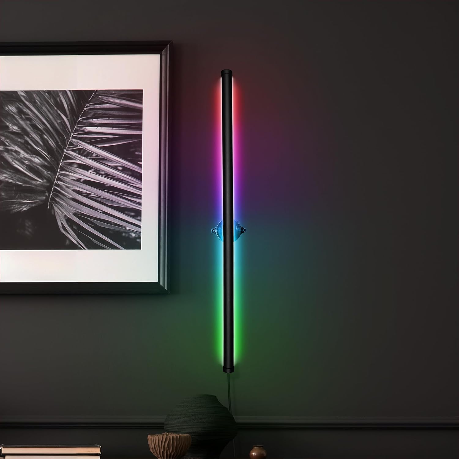 InnoVibe 28 inch Color Changing Wall Light Bar mounted vertically on a dark gray wall, displaying a rainbow of colors. A framed picture is to its left.
