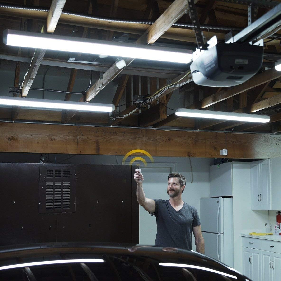 Man operating the Koda LED shop light with a remote control in a garage setting.