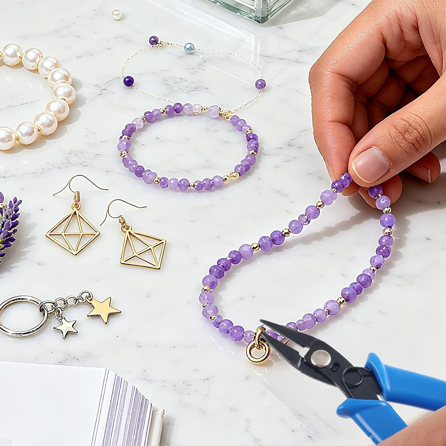 Hand using URSKYTOUS split ring pliers on a beaded bracelet surrounded by small findings and earrings