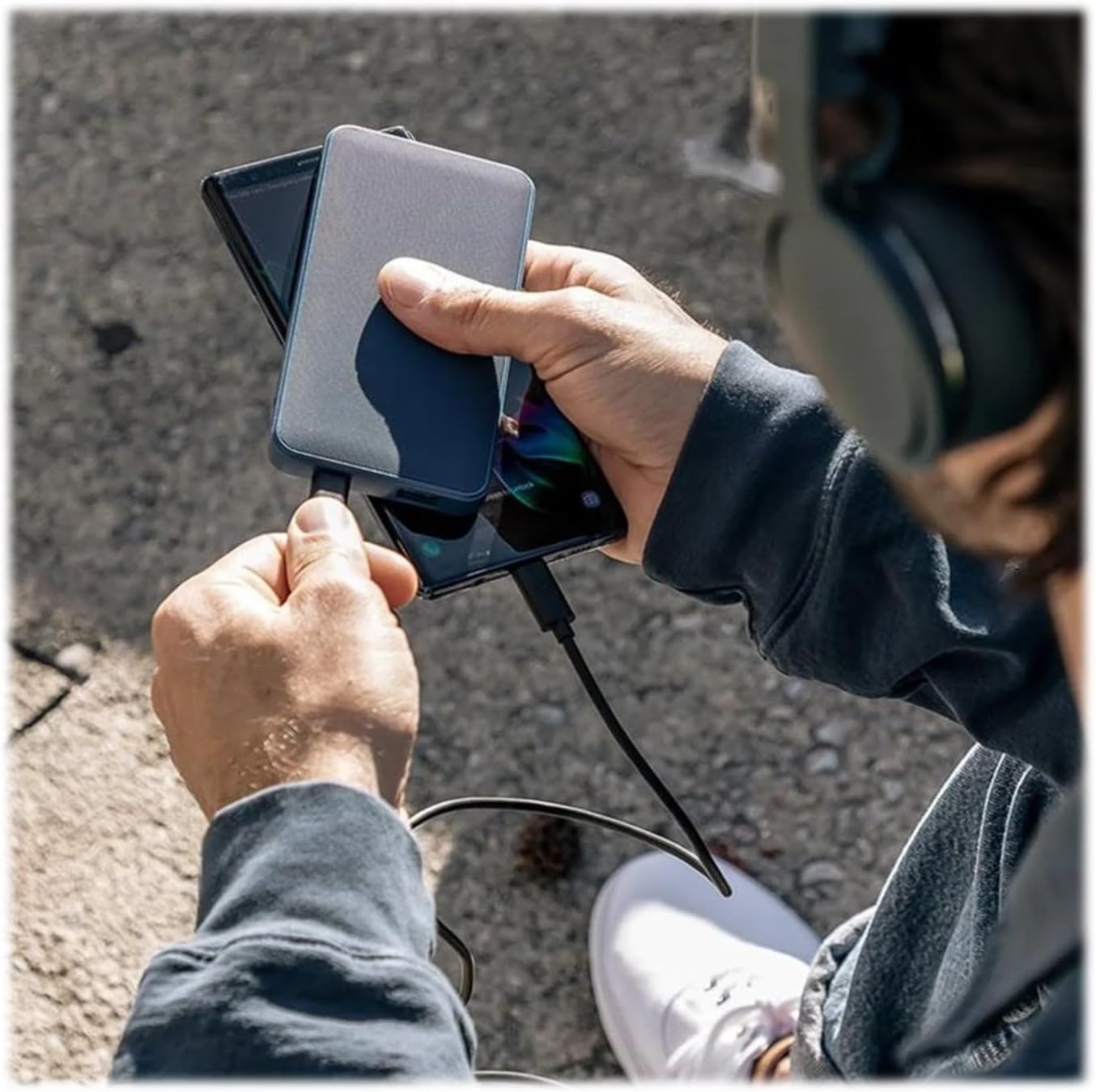 A person holding the Mophie powerstation and a smartphone, demonstrating simultaneous device charging.