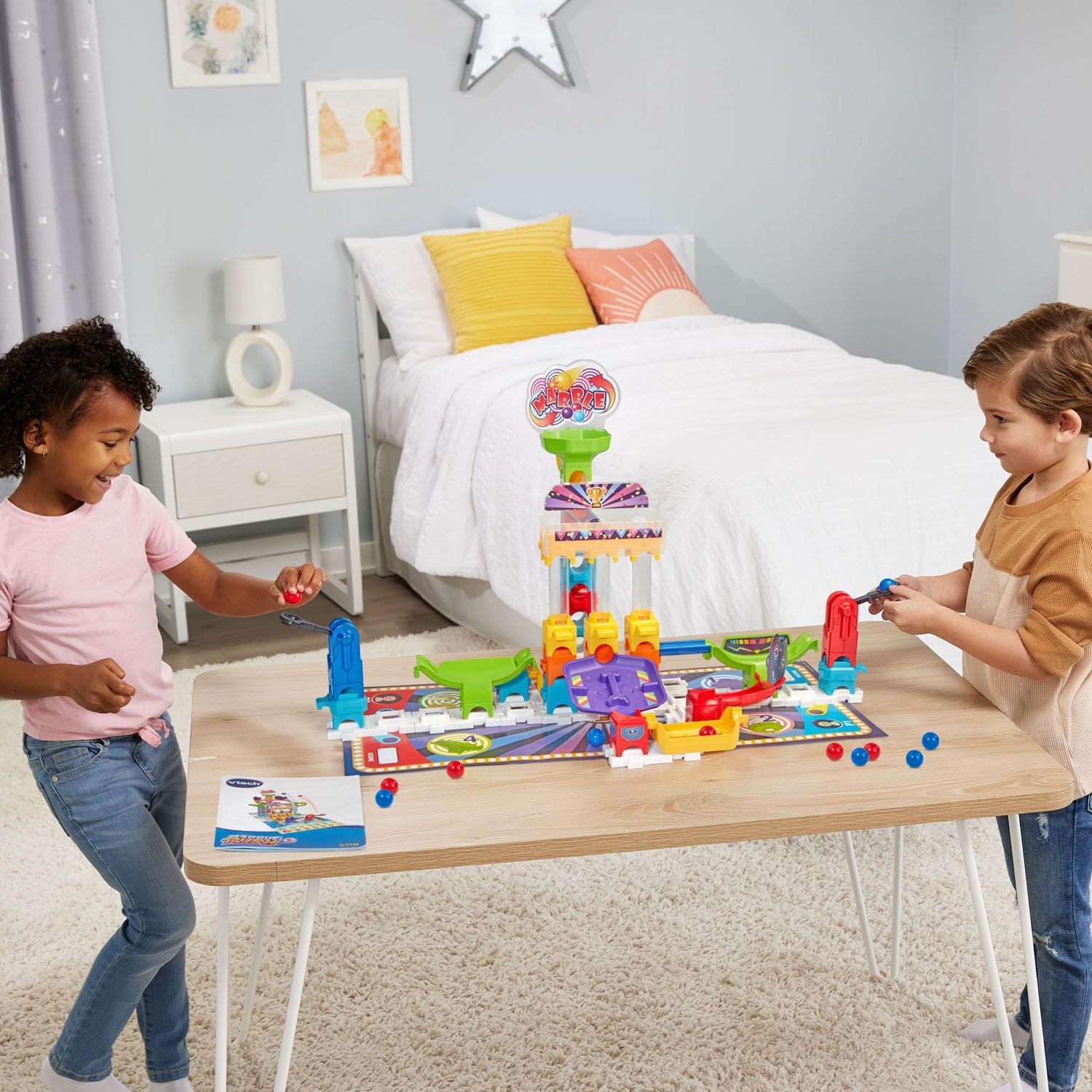 Two children are playing together with the VTech Marble Rush Carnival Challenge Game Set on a table, each interacting with different parts of the marble run.