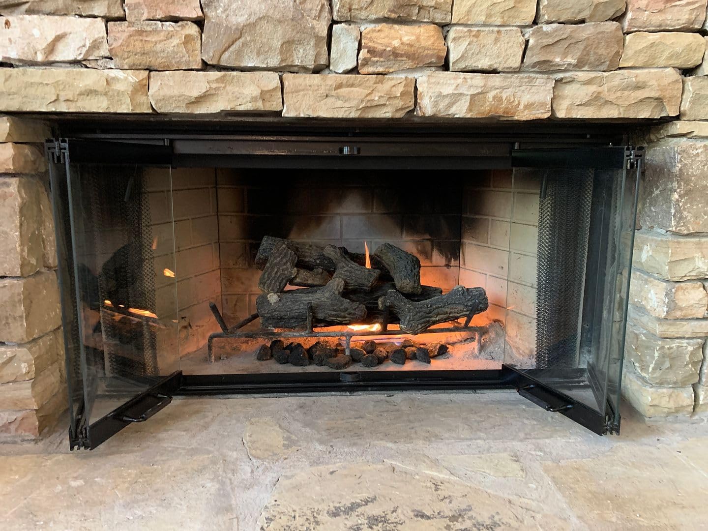 Fireplace glass doors with mesh screens open, showing a burning fire inside.