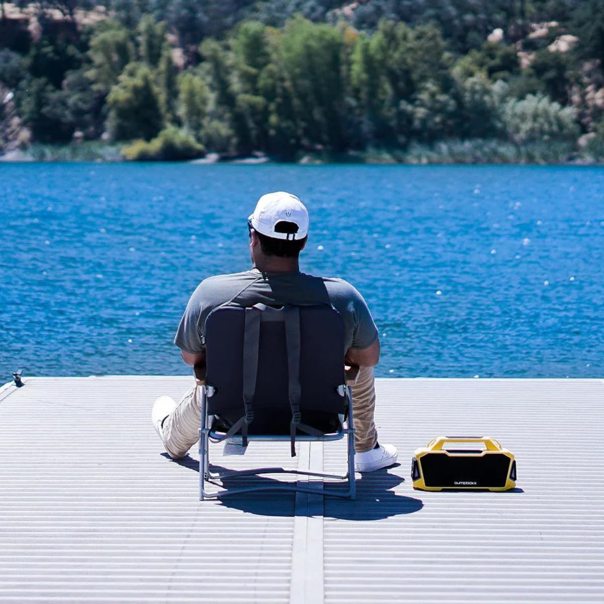 Person sitting by a lake with a Bumpboxx Thump speaker beside them
