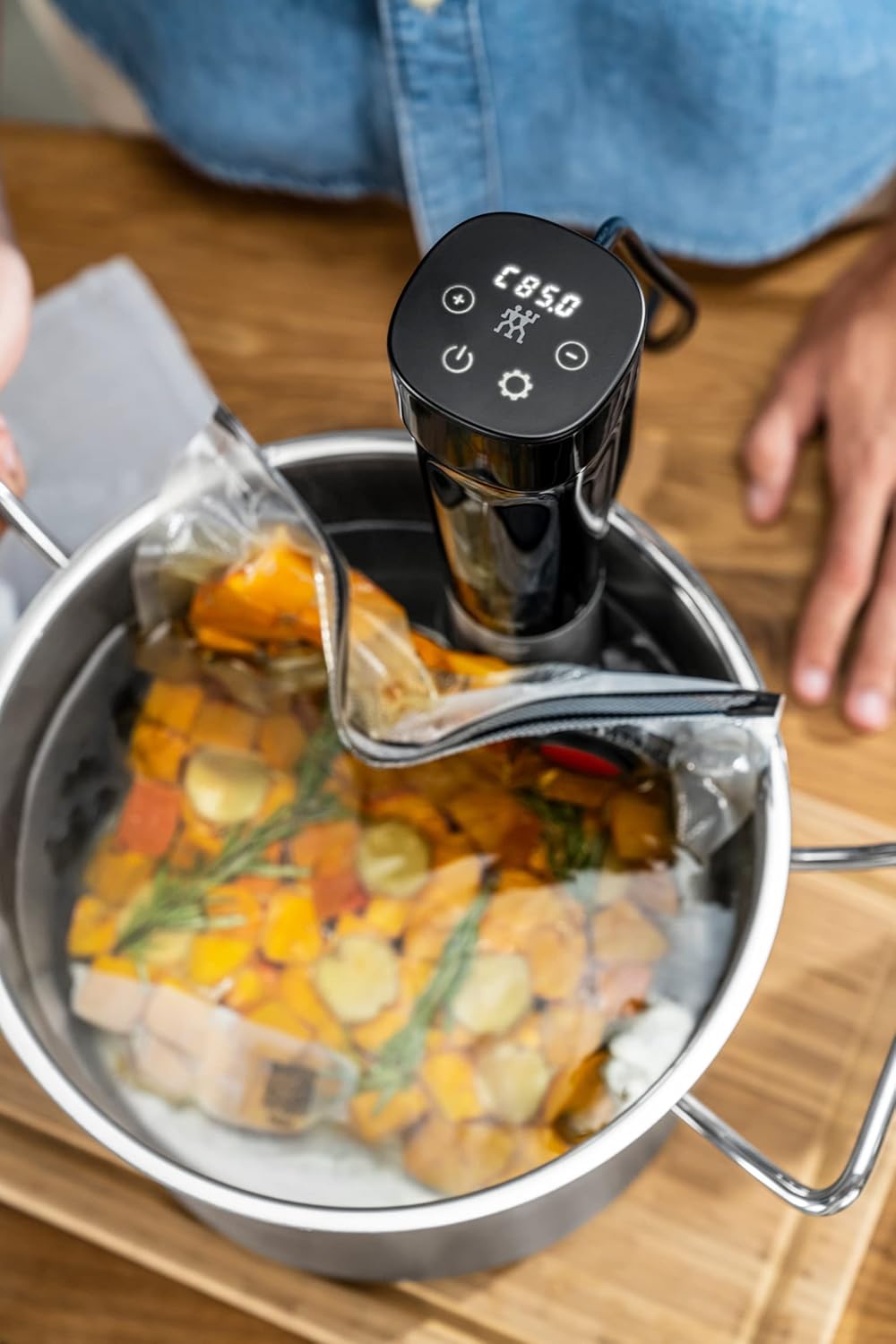 ZWILLING ENFINIGY Sous-Vide Cooker in use, with a vacuum-sealed bag of food submerged in a pot of water.