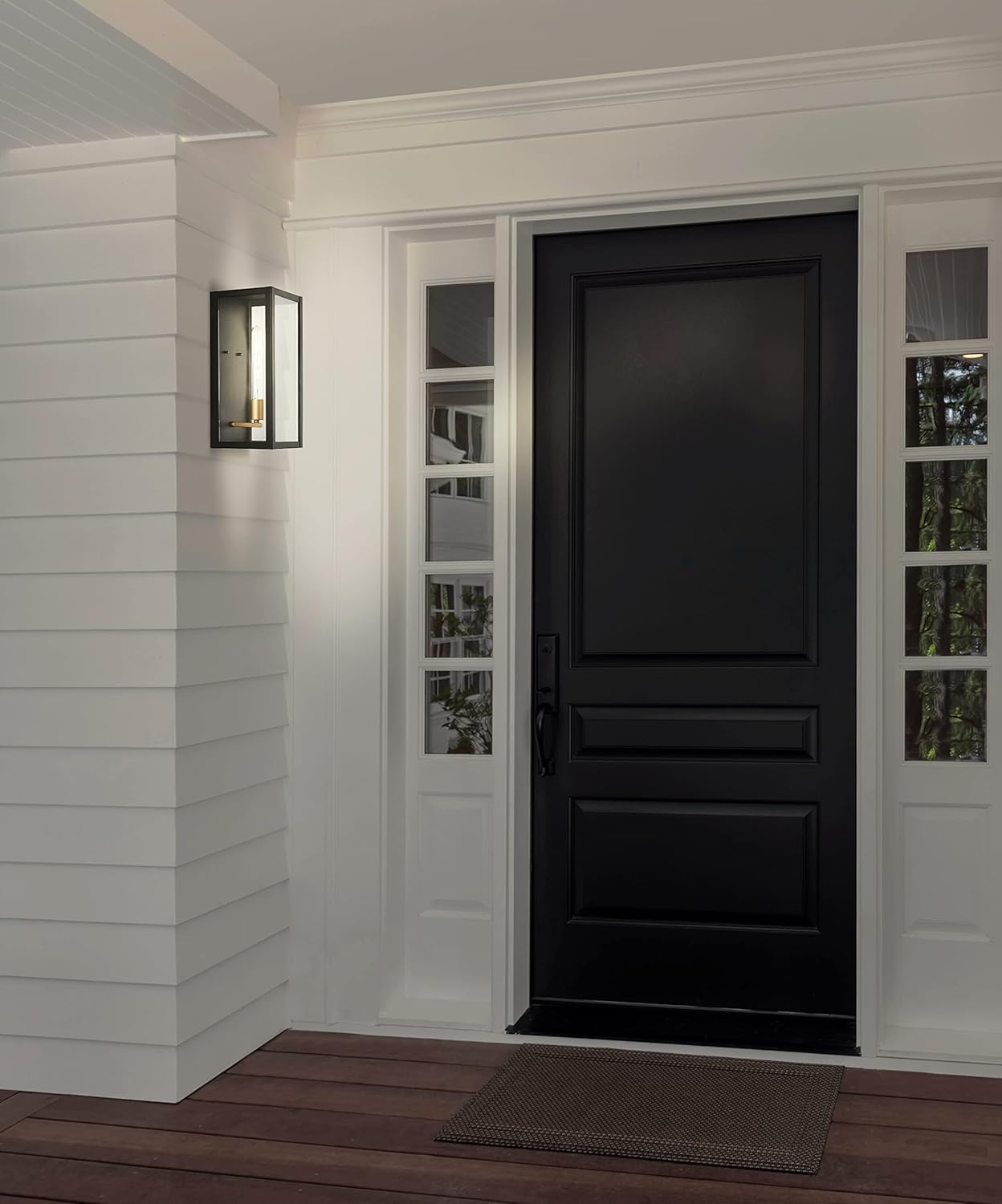 JONATHAN Y Berlin Outdoor Wall Lantern Sconce installed on a white exterior wall next to a black front door.