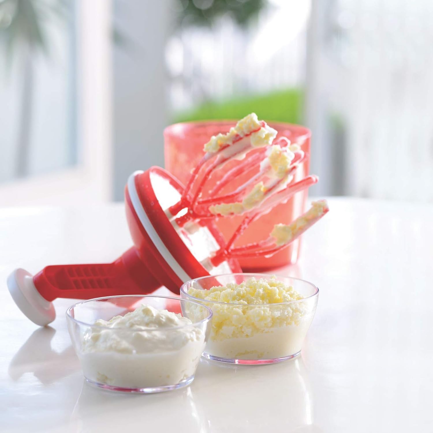 The whisk attachment from the Tupperware Speedy Chef, covered in churned butter, next to two small bowls containing whipped cream and freshly made butter.